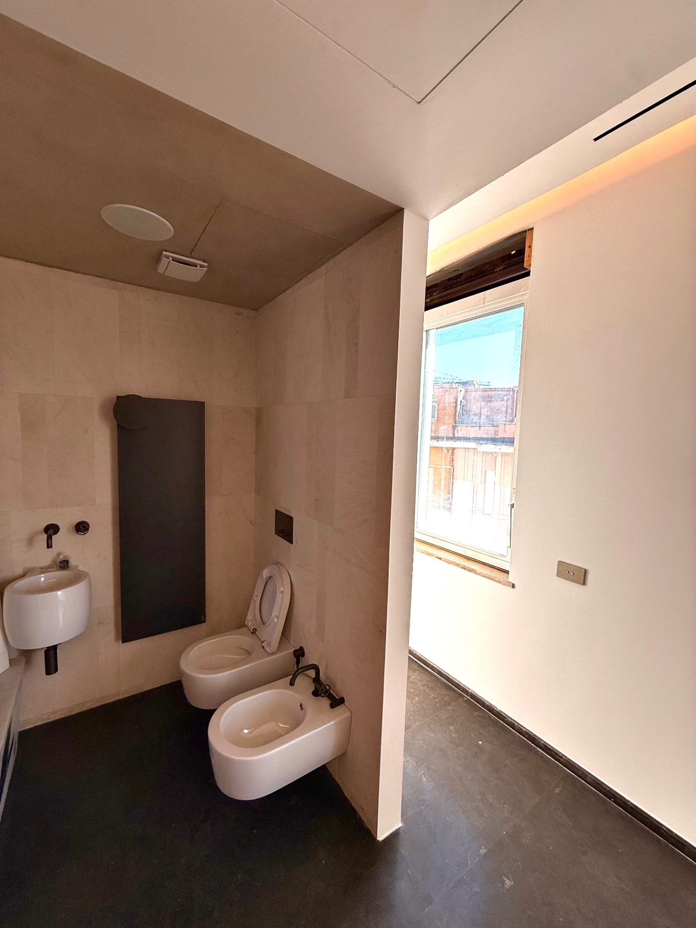Bagno in travertino con sanitari sospesi e rubinetteria nera